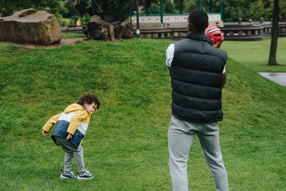 Father and son laughing while trying a partner yoga pose in the park